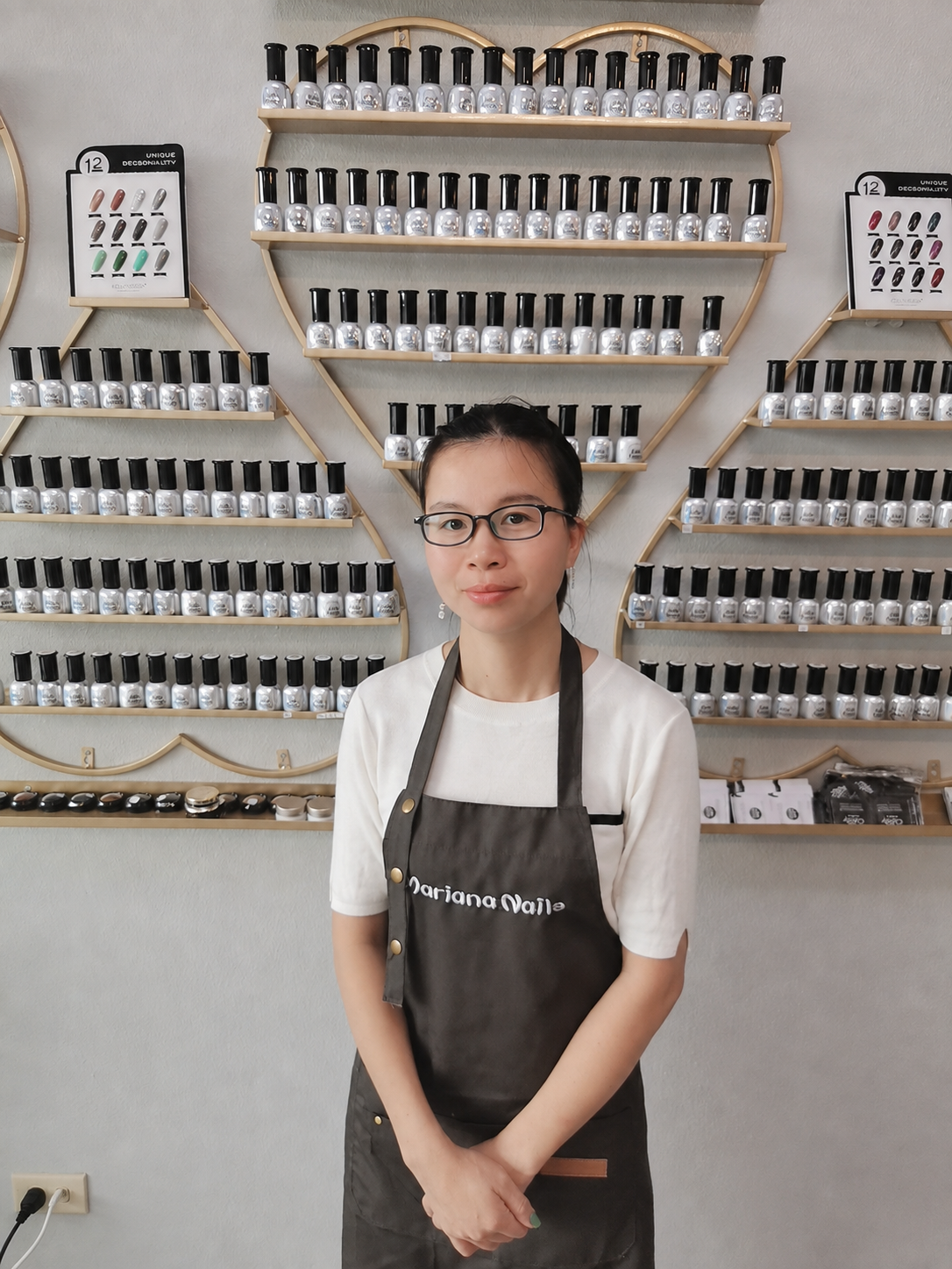 Mariana Nails nail technician standing in front of a wall display of nail polish colors at the salon in Saipan