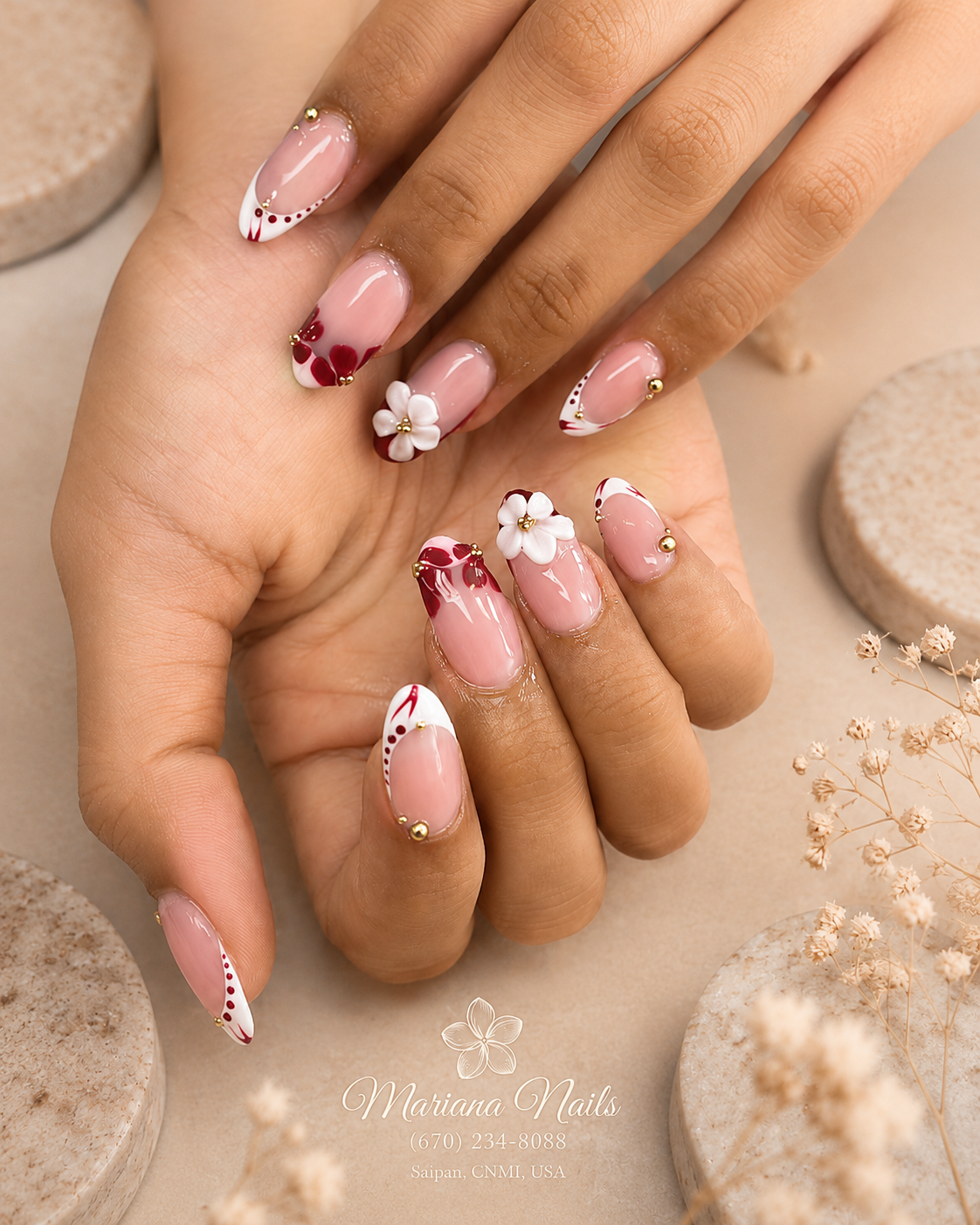 Glossy nude pink almond nails with red French-tip accents, 3D white flowers and gold details by Mariana Nails in Saipan